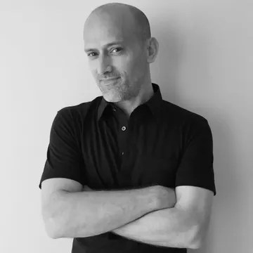 Portrait en noir et blanc d'un homme aux bras croisés, portant un polo noir.